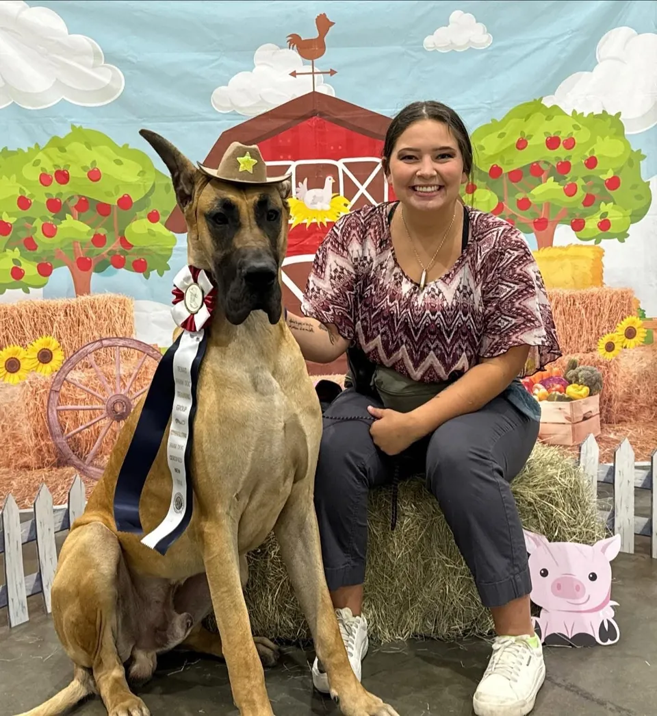 Blazer sitting with his owner in front of a farm-themed backdrop
